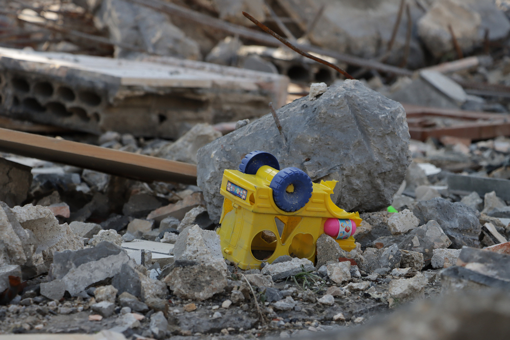 Yellow toy truck lies amidst rubble and debris / iStock/Ali Chehade Yellow toy truck lies amidst rubble and debris, symbolizing destruction and abandonment in a chaotic, post-disaster urban environment. impact of disasters on everyday life, or the loss of innocence.